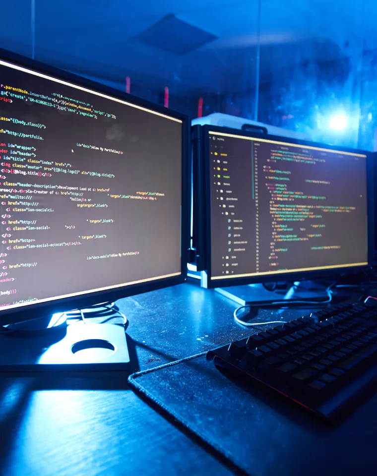 Application Software Development: monitors displaying code in a blue-lit workspace