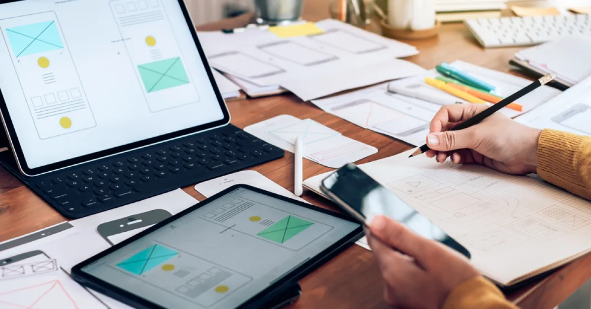 How AI Is Changing Custom Application Development in 2026: designer sketching mobile app wireframes beside a tablet