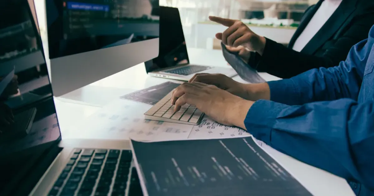 Custom Application Development vs. Off-the-Shelf Software: Which One Is Right: hands typing on a laptop beside a colleague